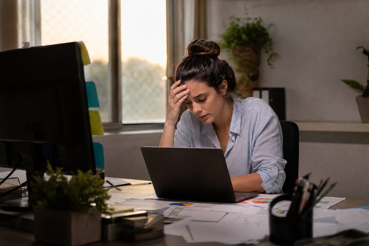 Assistente de backoffice revisando relatórios impressos ao lado do notebook